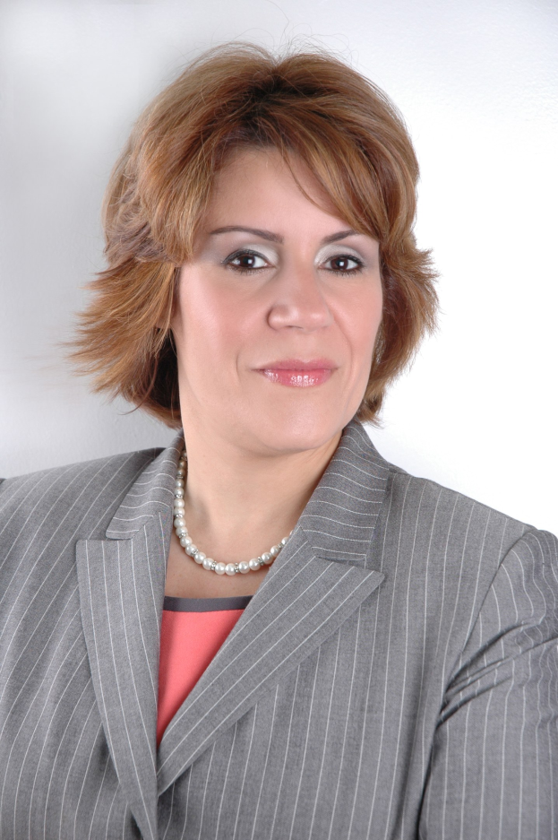 Eine selbstbewusste Frau in einem marineblauen Businessanzug mit weißem Hemd und gemustertem Schlips steht aufrecht vor einem weißen Hintergrund, ihre Haltung und direkter Blick vermitteln professionelle Stärke.