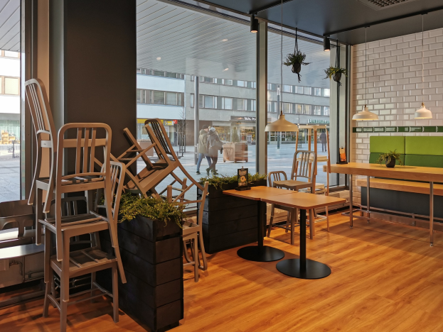 Ein Berliner Restaurant mit Holztischen und -stühlen vor einem großen Fenster, das auf eine Straße mit Fußgängern, Gebäuden und urbanen Elementen blickt.