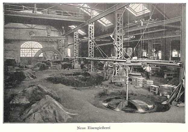 Schwarzes und weißes Foto eines Fabrikinneren mit Arbeitern, die an Maschinen arbeiten, Metallstangen und -rohre sowie die Beschriftung 'Neue Eisenglebeerei, die erste Fabrik in Deutschland' am unteren Rand.